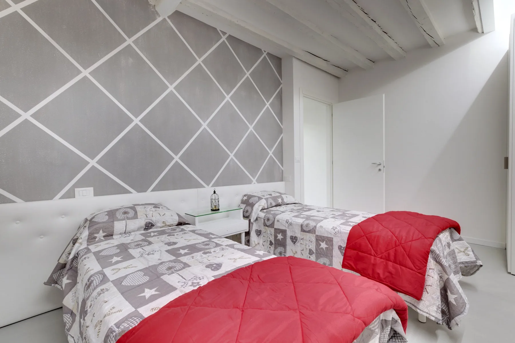 Bedroom with two beds dressed in patterned bedding and red quilts.