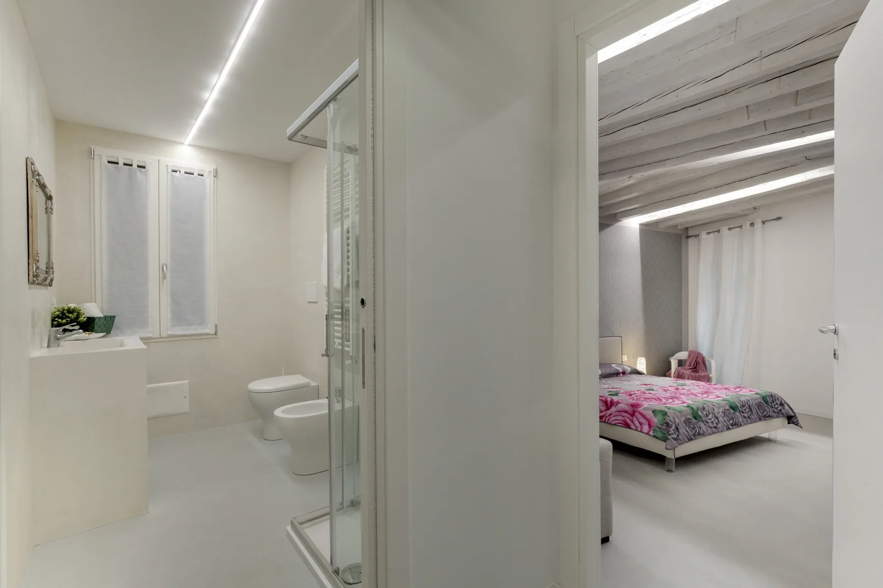 A bright bathroom opens onto a bedroom with a pink floral bedspread.