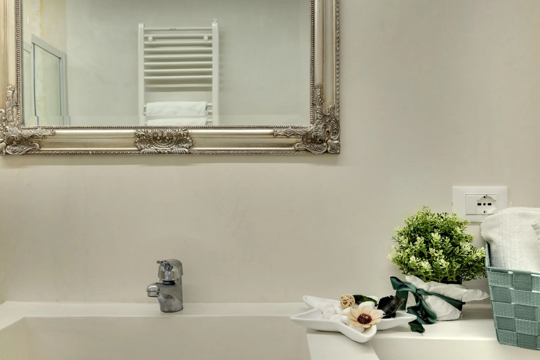 A bathroom vanity with a wall mirror, faucet, and small decorative arrangement.
