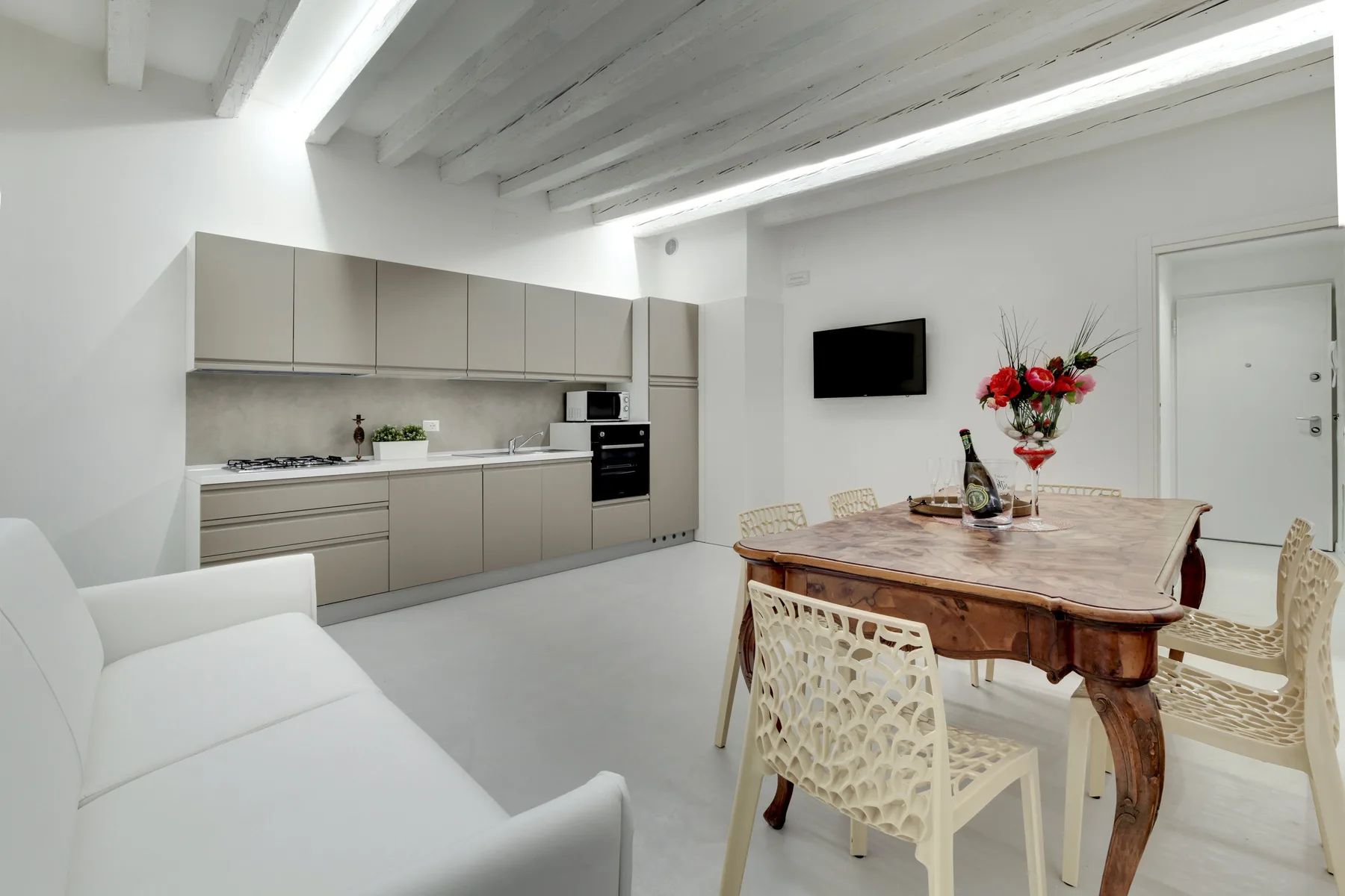 A bright open-plan kitchen and dining area with pale cabinetry and a wooden table.
