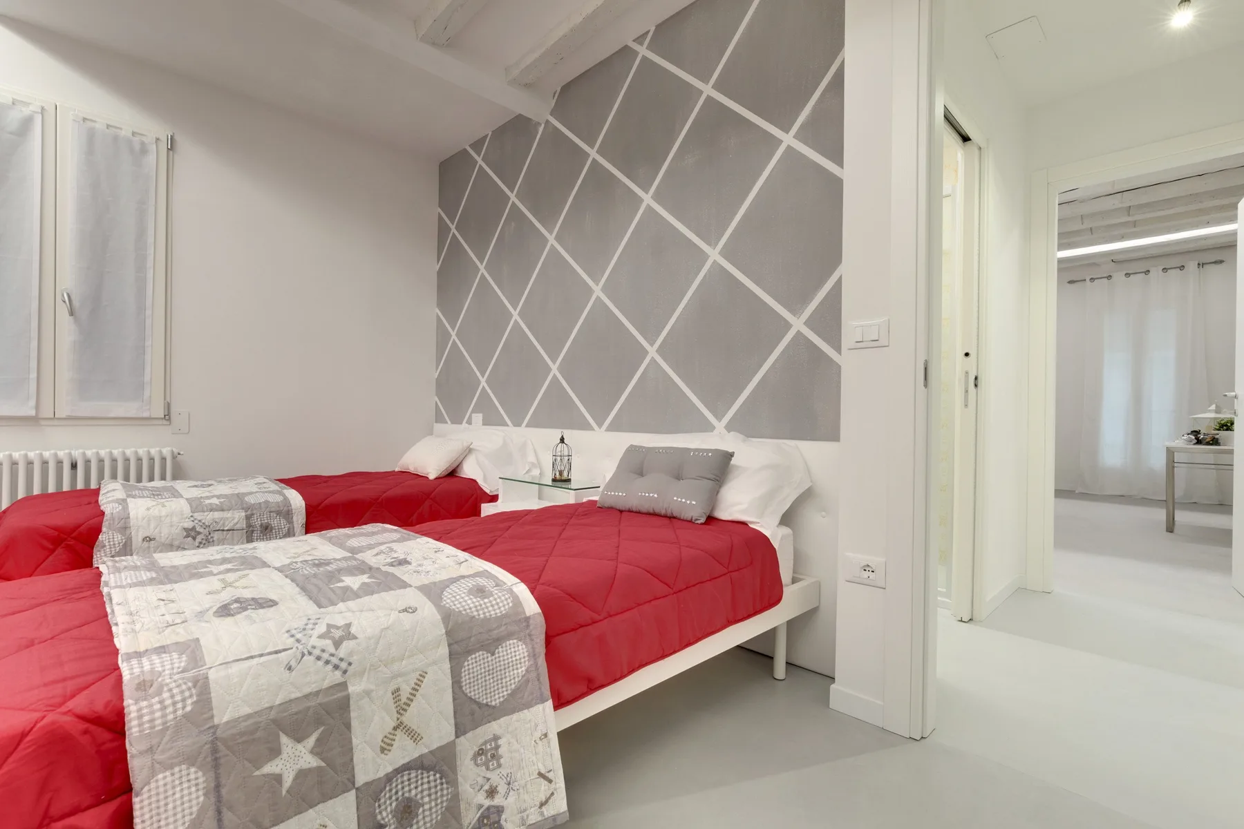A bedroom with red bedding and a gray geometric accent wall.