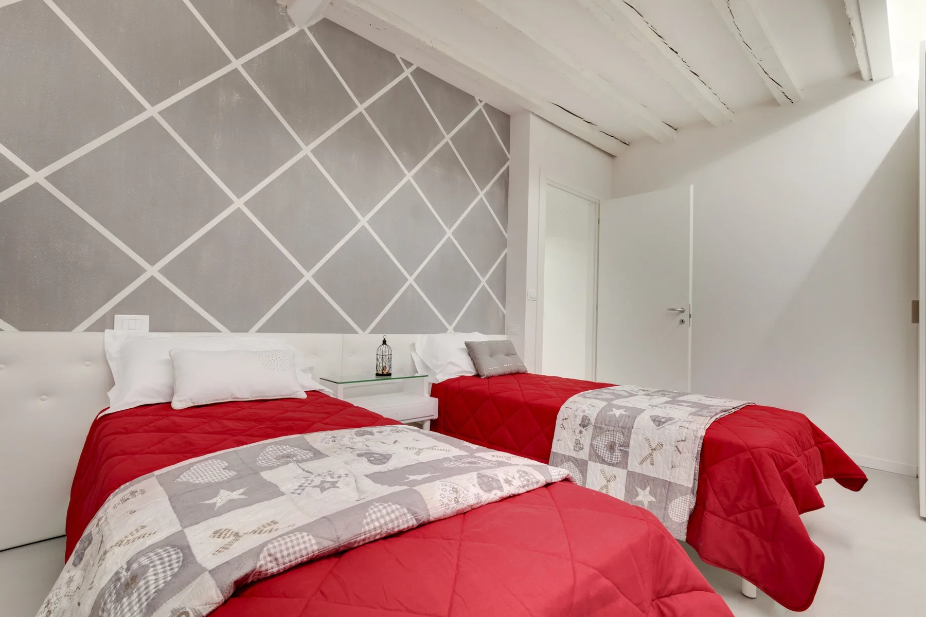 A bedroom with two beds dressed in red bedding and patterned throws.