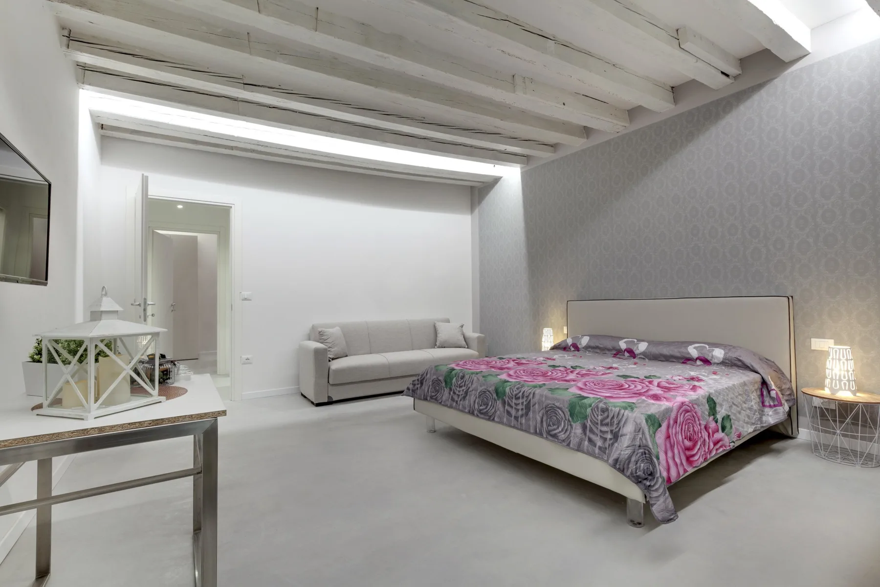 Un dormitorio con una cama cubierta con una colcha floral y un sofá cercano.