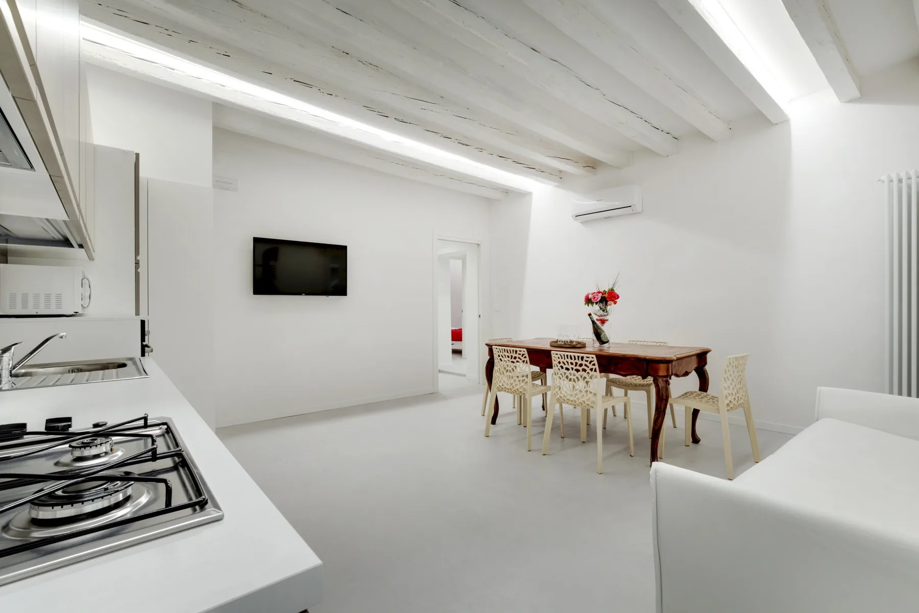 A bright dining area with a wooden table and chairs beside a compact kitchen.