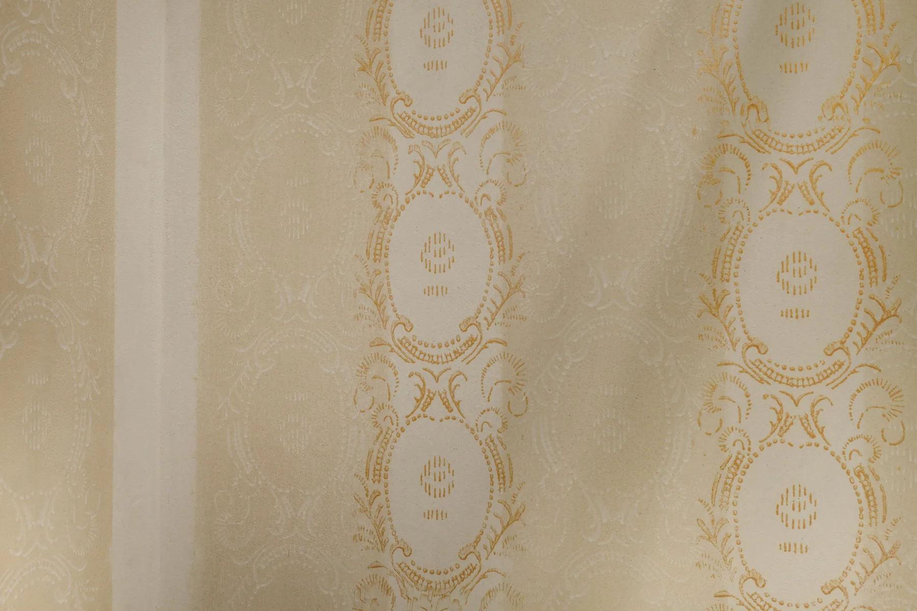 A close-up of cream curtains with ornate gold patterns.