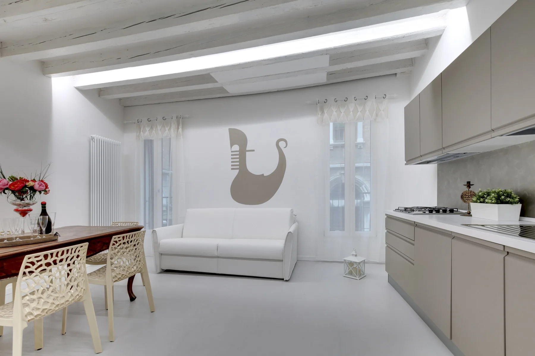 A bright open-plan room with a white seating area beside a dining table and kitchen.