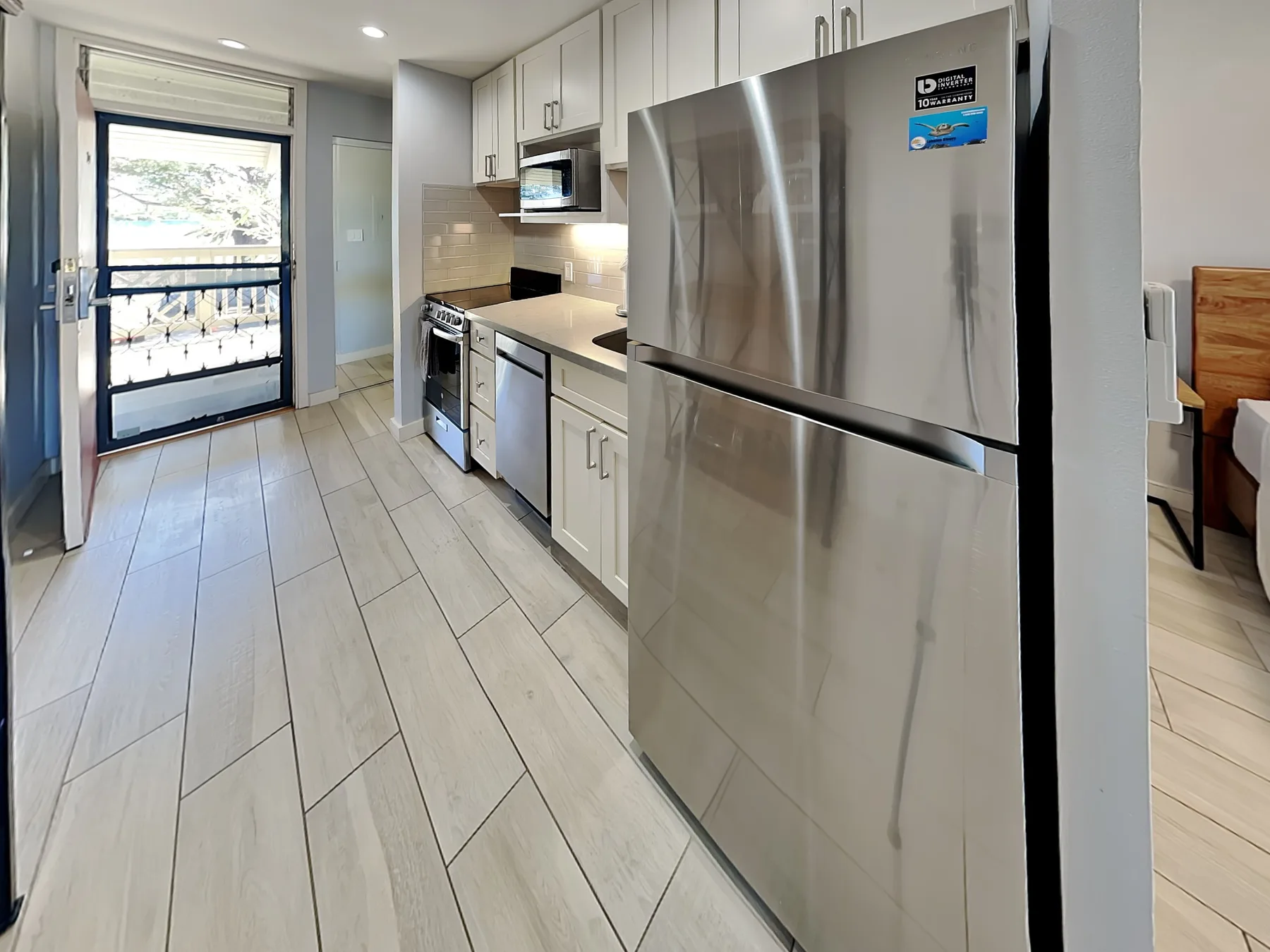 A compact kitchen with white cabinets, stainless steel appliances, and a glass door.