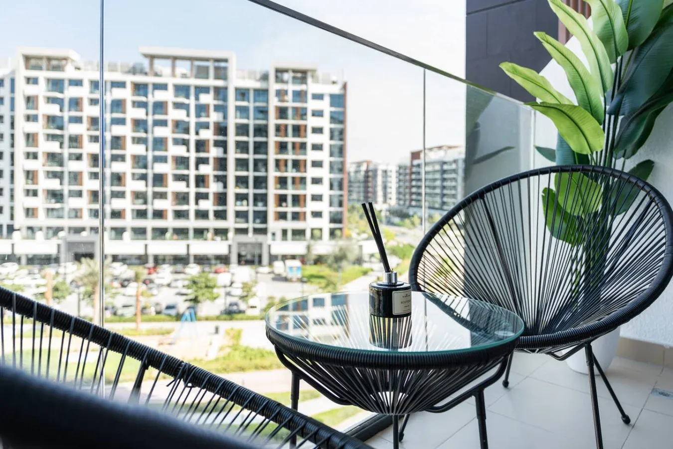 Una zona de estar en el balcón con una mesa de vidrio y edificios cercanos a la vista.