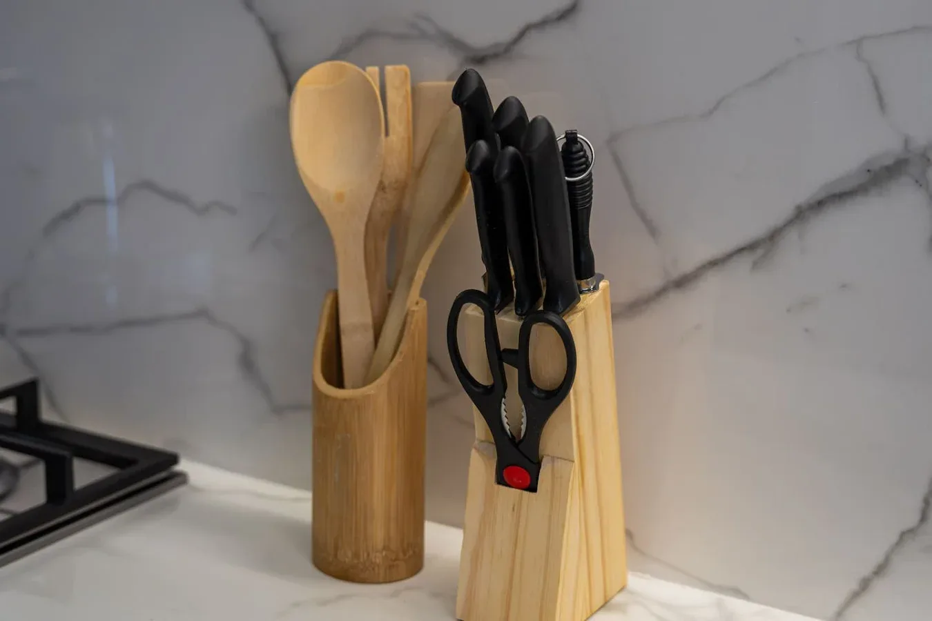 Utensilios de cocina y tijeras están sobre una encimera junto a un salpicadero jaspeado.