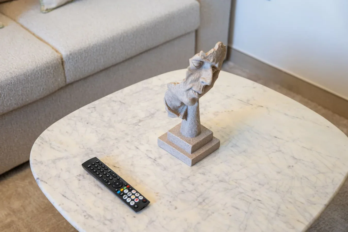 Una zona de estar con un busto escultórico y un control remoto sobre una mesa de centro.