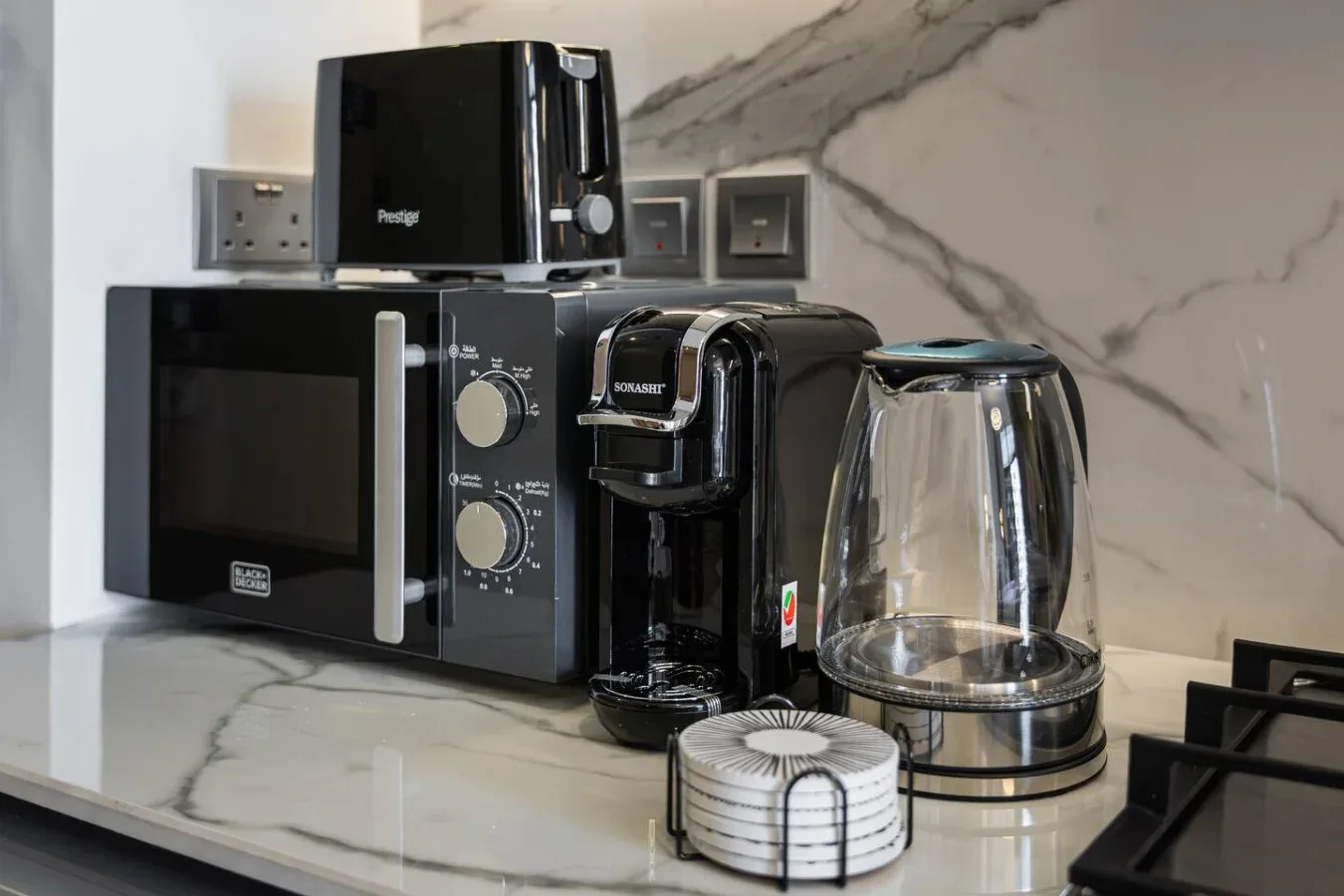 Una encimera de cocina tiene un microondas, una cafetera, un hervidor y pequeños electrodomésticos.