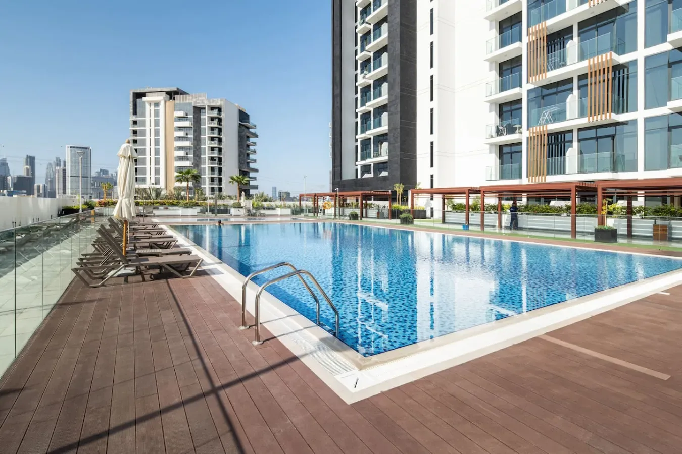 Una piscina al aire libre junto a edificios modernos de gran altura, con asientos en la terraza.