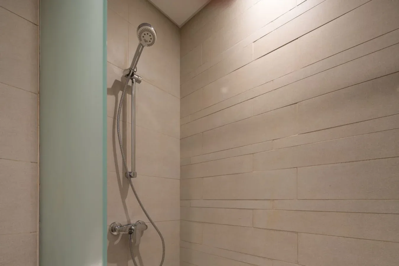 Una ducha revestida de azulejos con ducha de mano y mampara de vidrio.