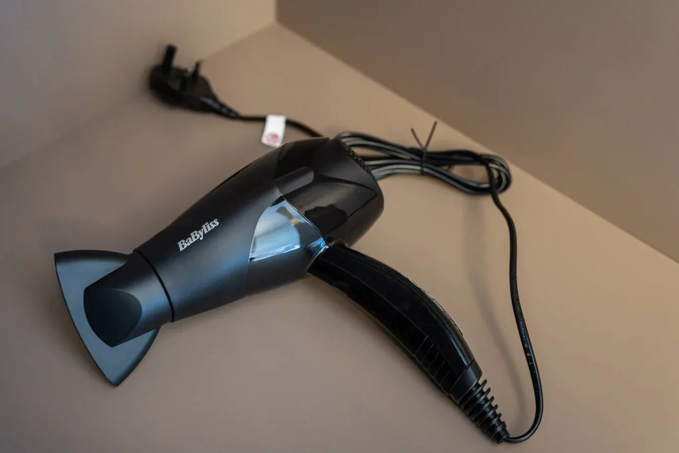 Un secador de pelo está sobre una encimera, con el cable de alimentación enrollado al lado.