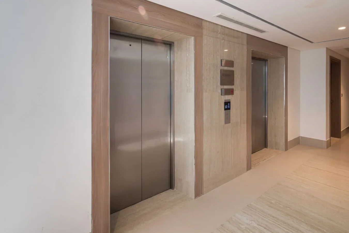 Vestíbulo interior de ascensores con puertas metálicas y un suelo de baldosas claras.