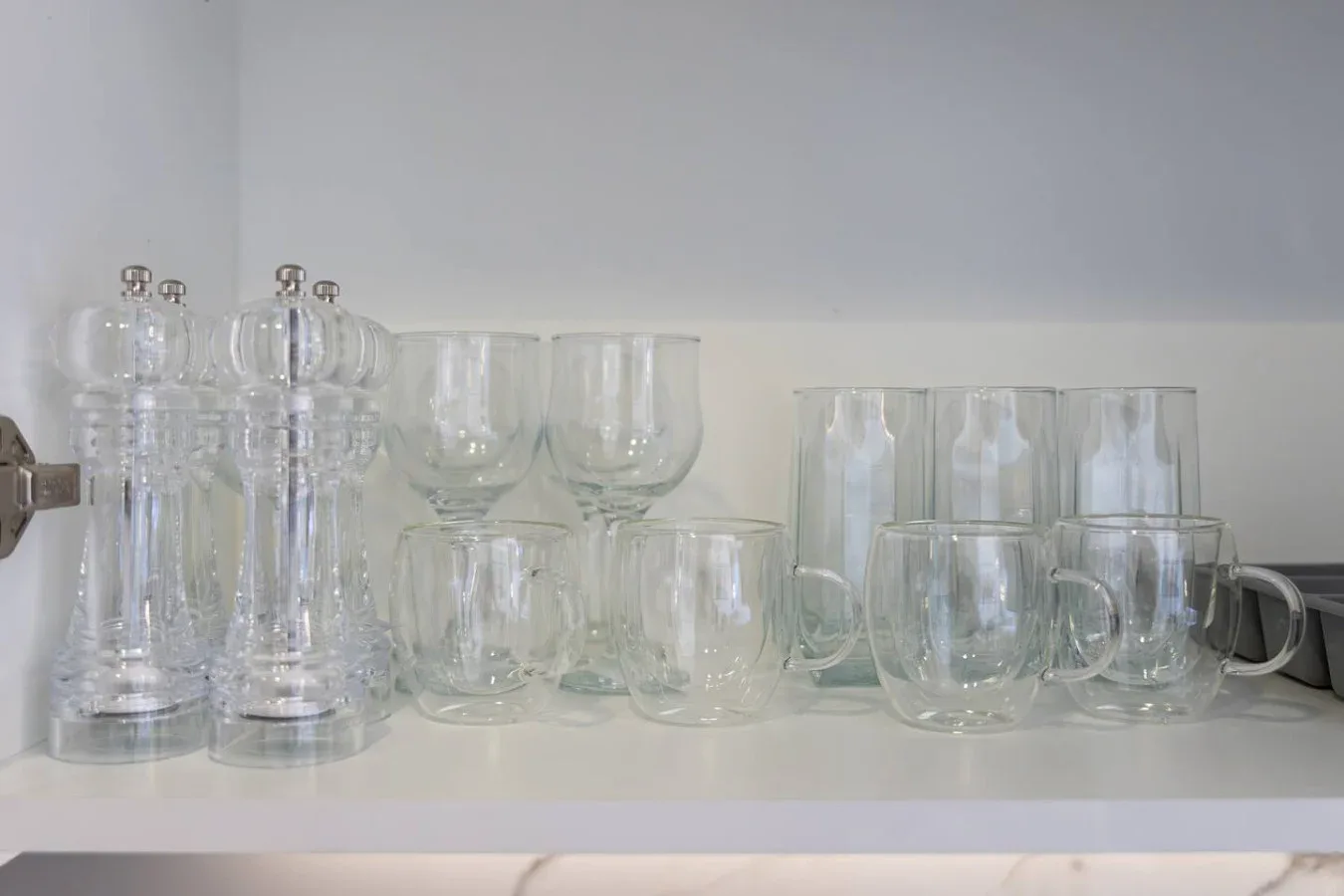 Un estante de armario contiene varios vasos y tazas de vidrio transparente.