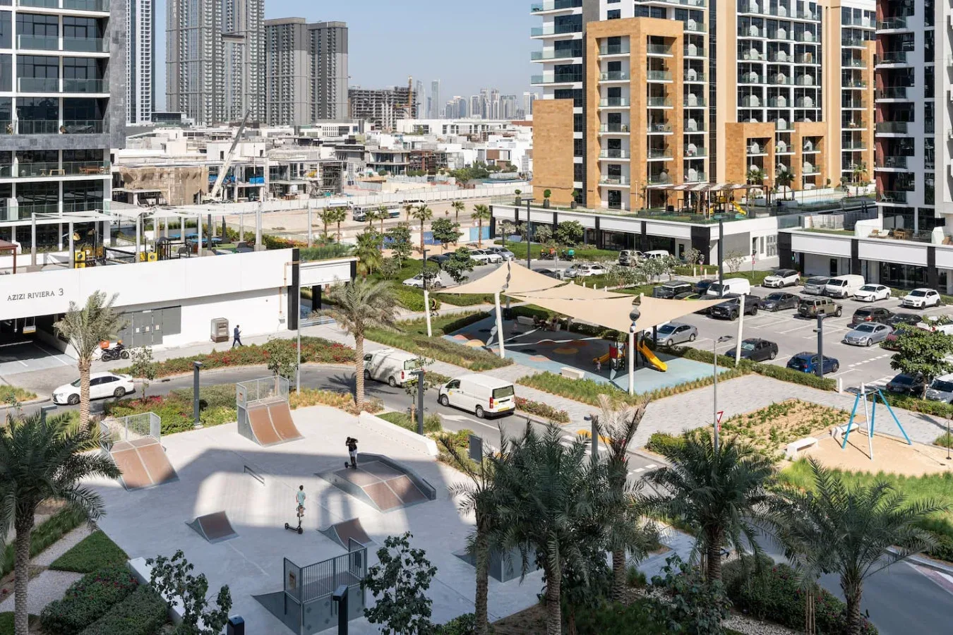 Un complejo residencial ajardinado con zona de juegos, estacionamiento y edificios altos alrededor.