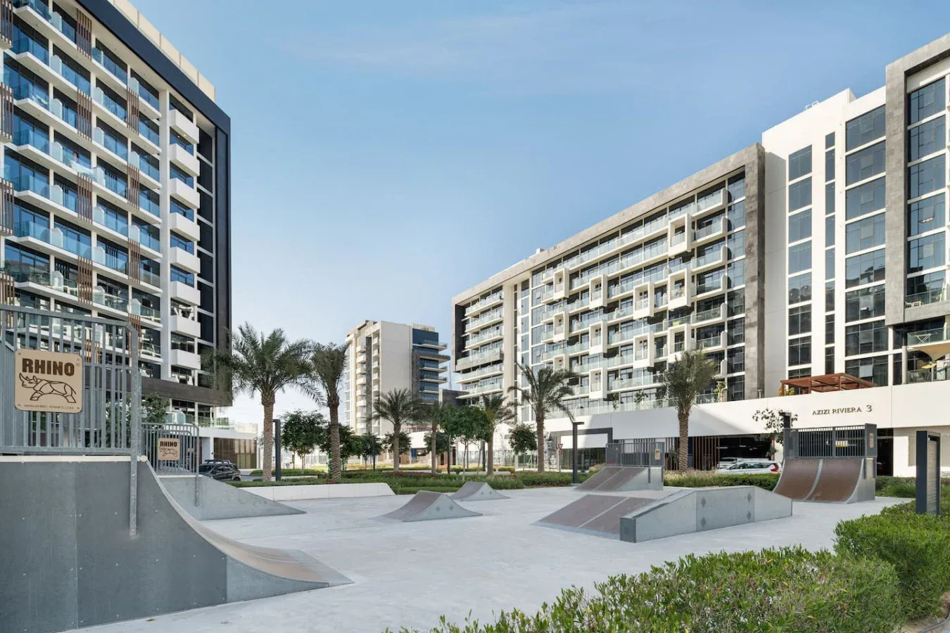 Un parque de skate con rampas está entre edificios de apartamentos modernos y palmeras.