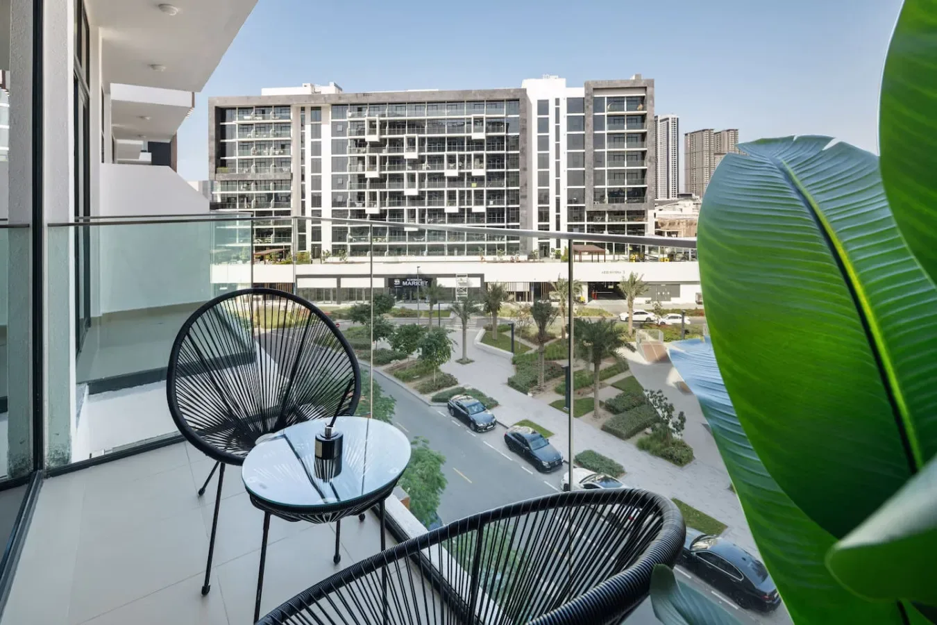 Una zona de estar en un balcón da a un patio ajardinado y edificios cercanos.