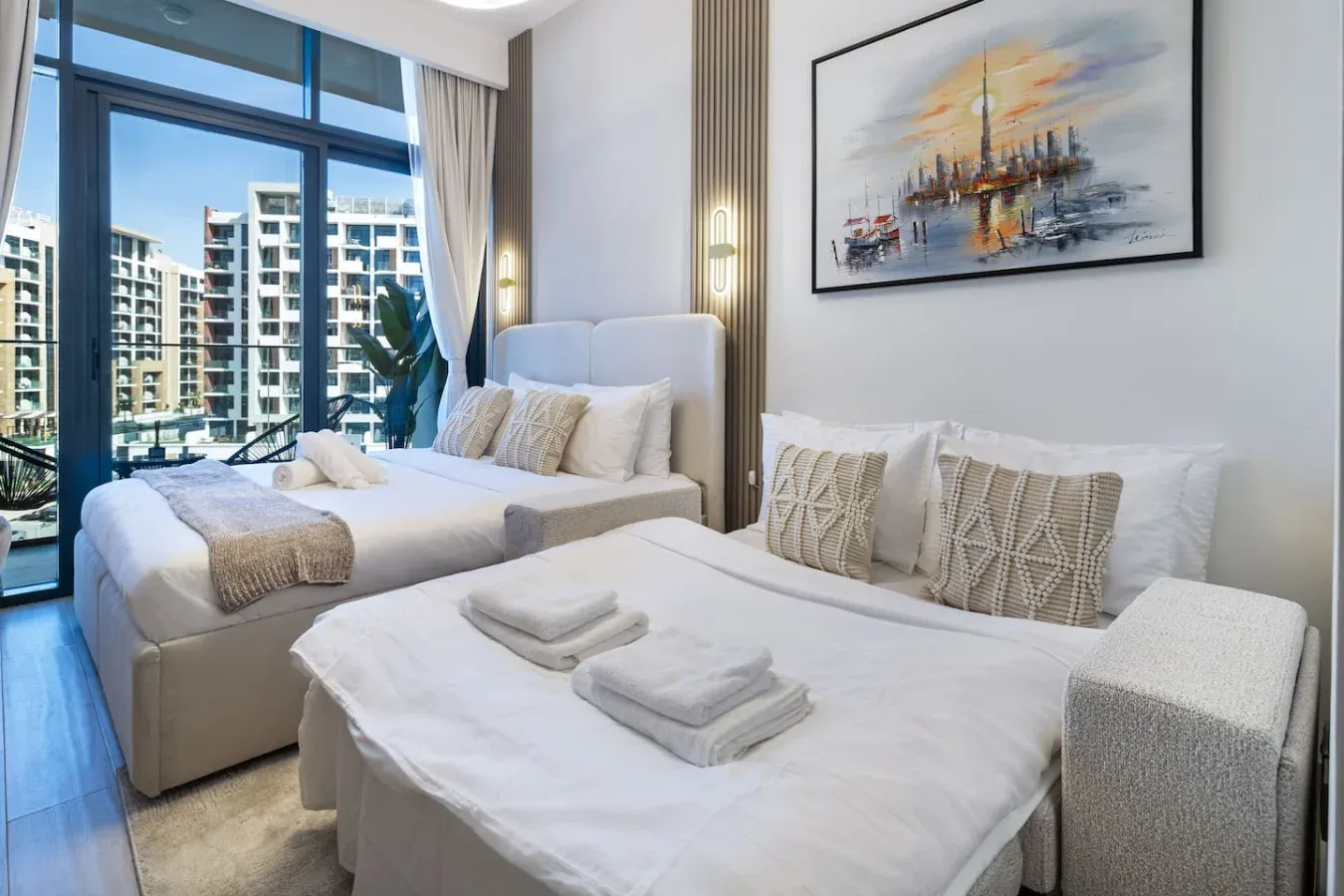 Un dormitorio luminoso con dos camas, ropa de cama neutra y grandes ventanas.