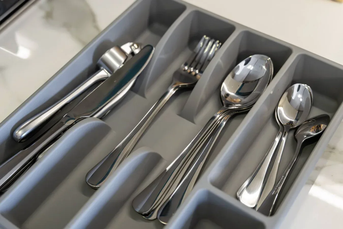 Un organizador de cajón de cocina contiene cubiertos y utensilios de servir ordenados.