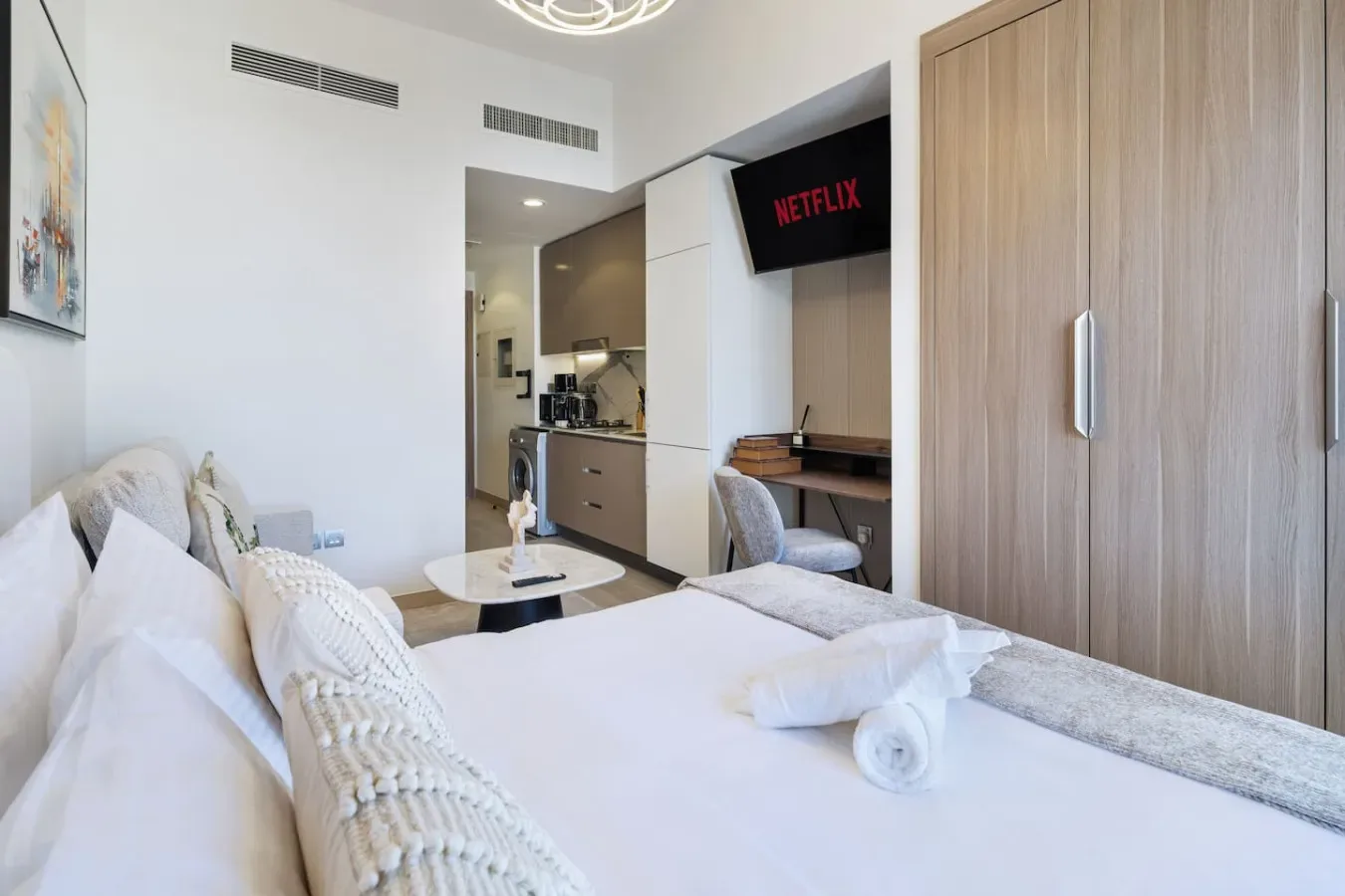 Un dormitorio luminoso con cama, asientos y una pequeña cocina.