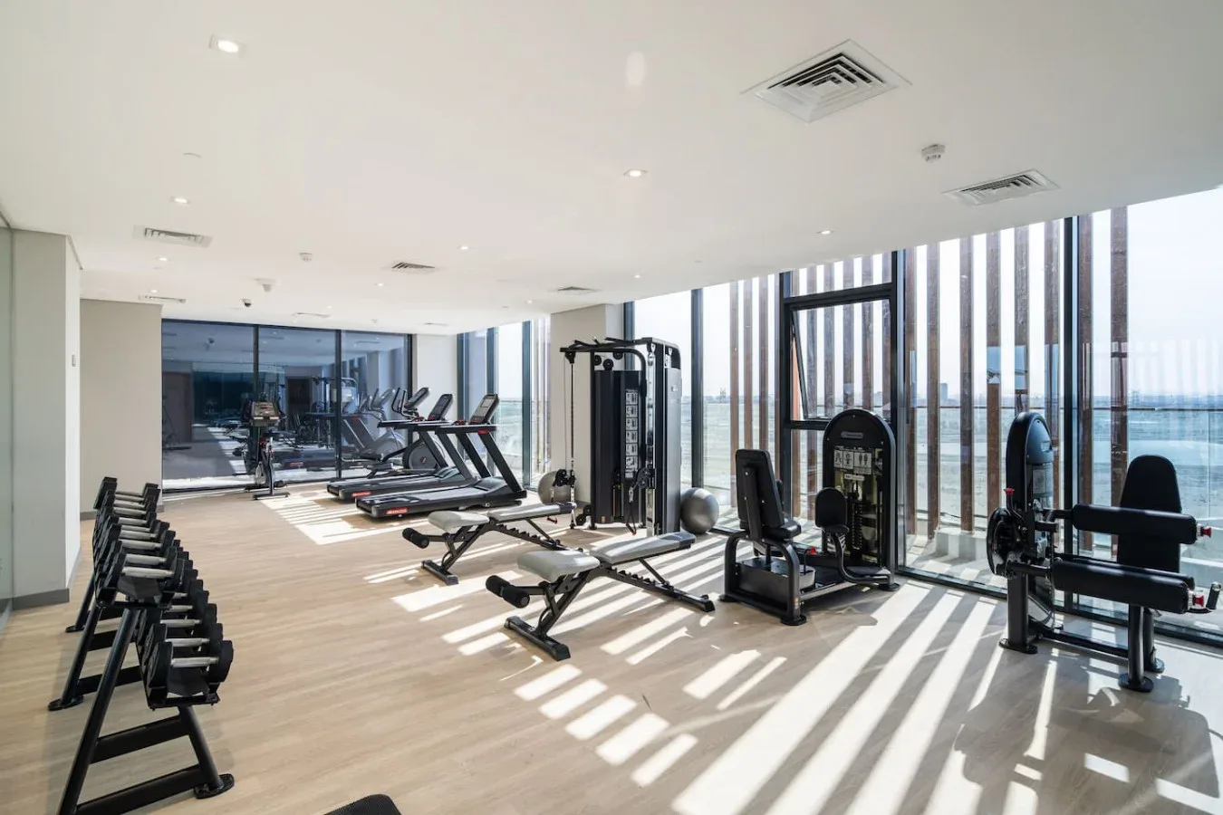 Un gimnasio luminoso con equipos de ejercicio junto a ventanas altas.