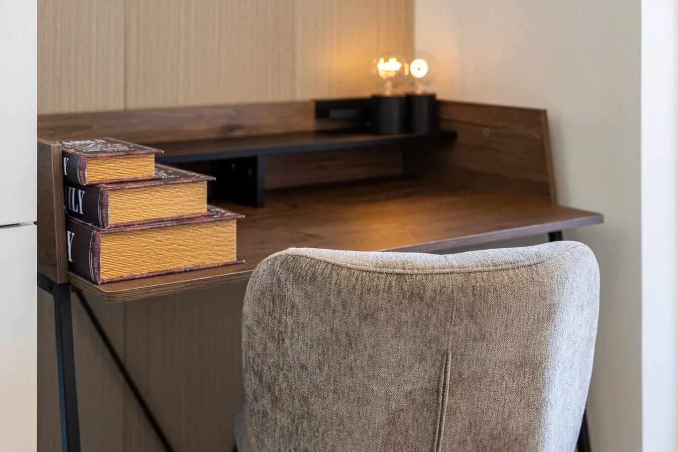 Un escritorio con una silla acolchada y libros apilados está junto a la pared.