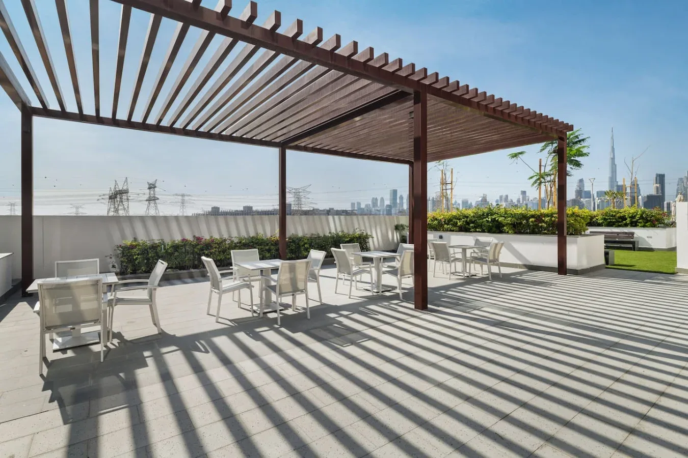 Una terraza en la azotea tiene asientos al aire libre bajo una pérgola de madera, con el horizonte de la ciudad al fondo.