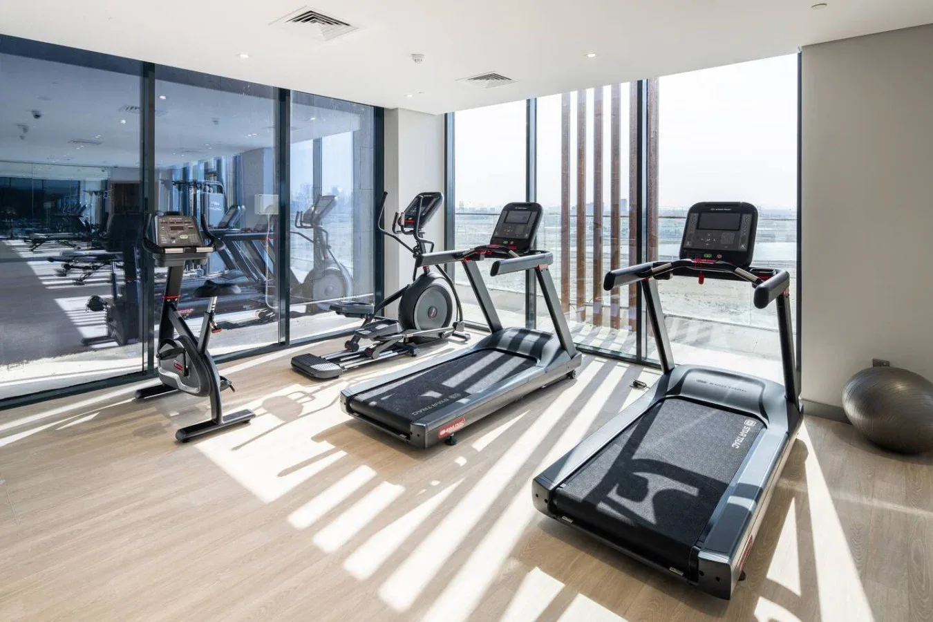 Un gimnasio luminoso con cintas de correr y bicicletas estáticas junto a ventanales.