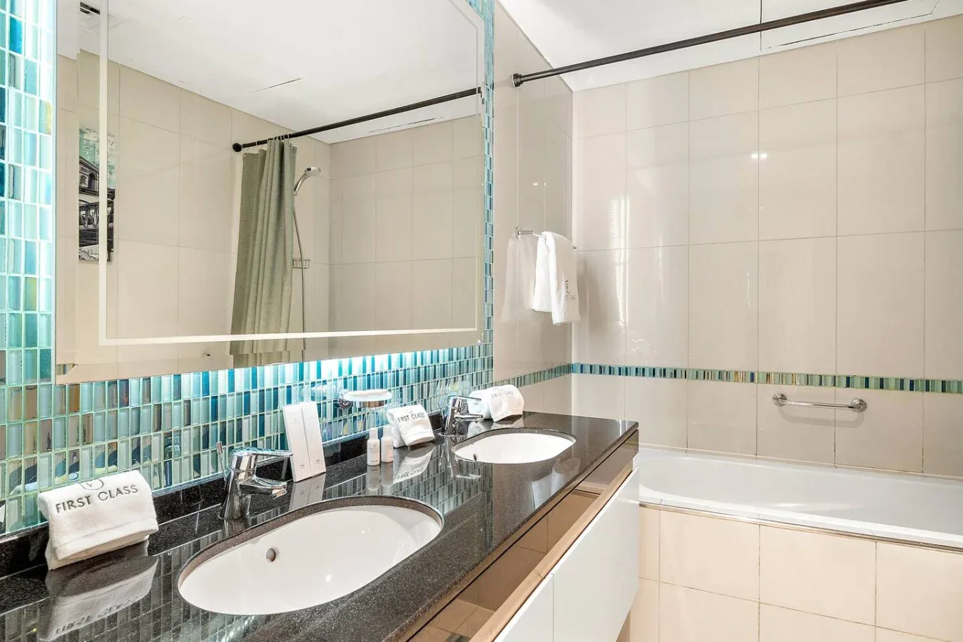Un baño alicatado con un lavabo largo, dos lavabos y una bañera.