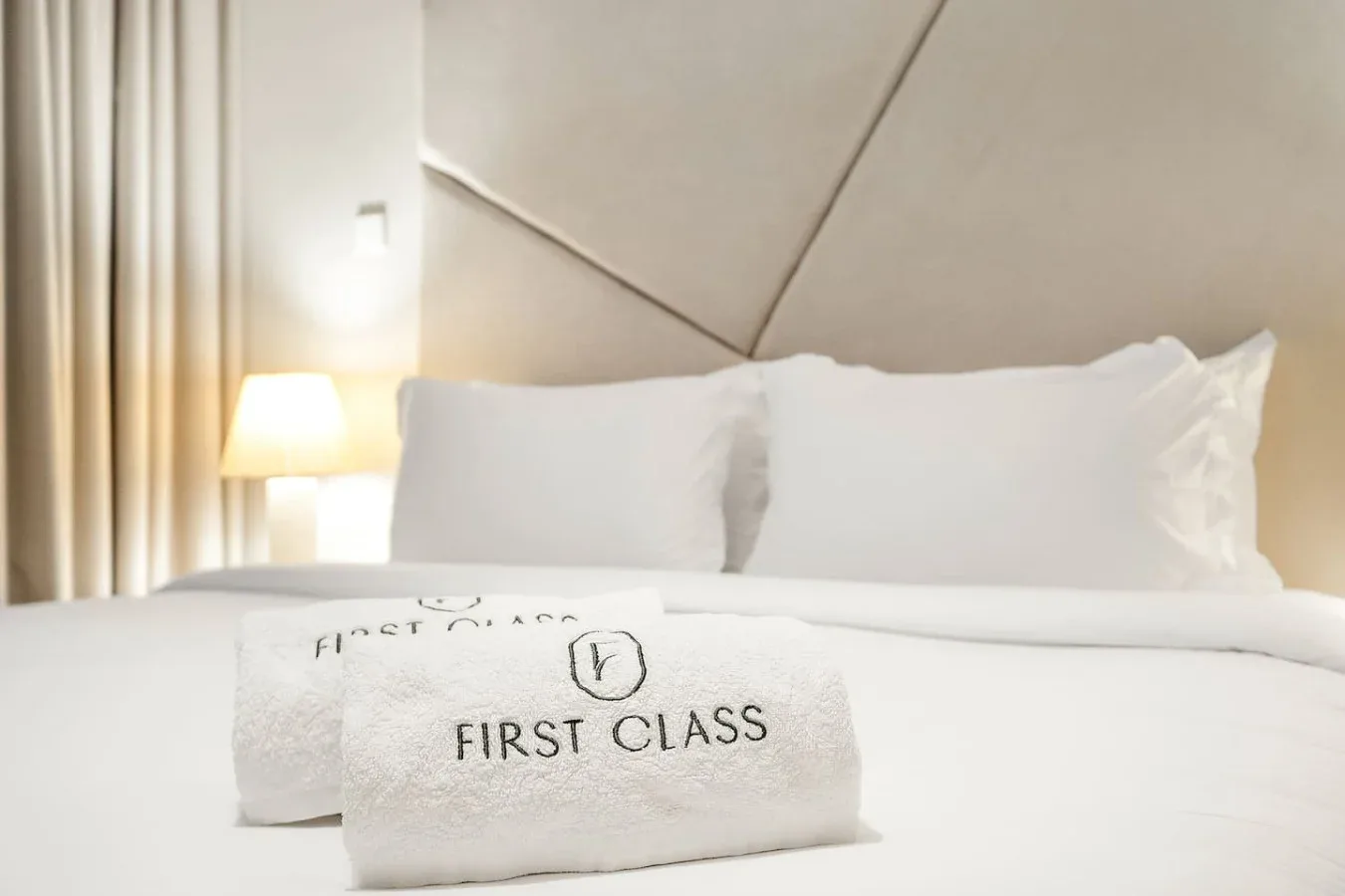 Una cama bien hecha con almohadas blancas y una toalla doblada en primer plano.