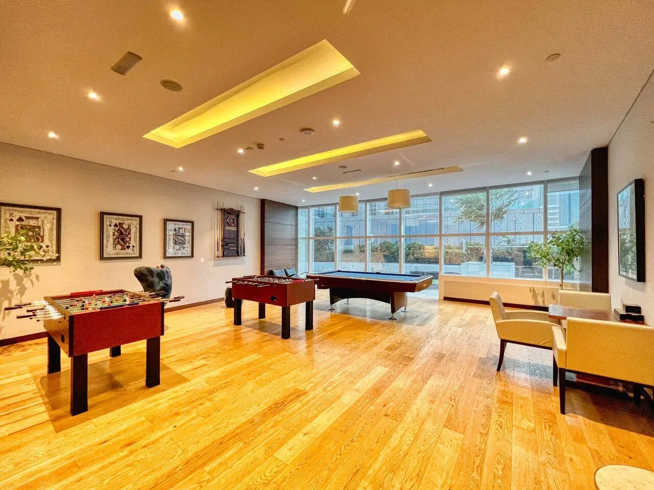 Una luminosa sala de juegos con mesas de billar, futbolín y asientos junto a grandes ventanales.