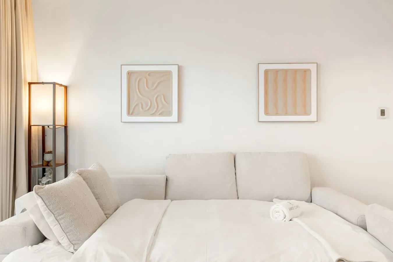 Una sala luminosa con asientos claros, cuadros enmarcados y una lámpara de pie.
