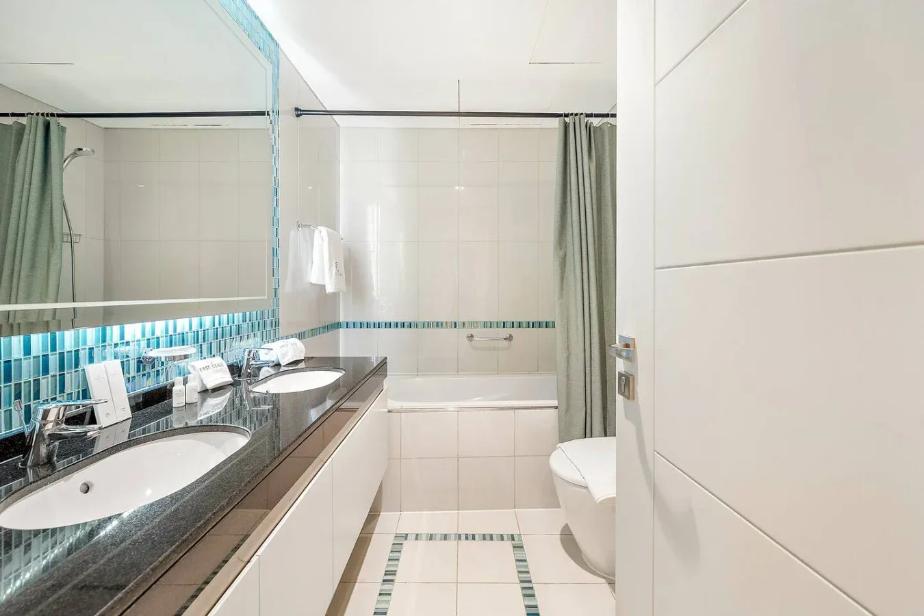 Un baño con azulejos, un lavabo largo, bañera y cortina de ducha.
