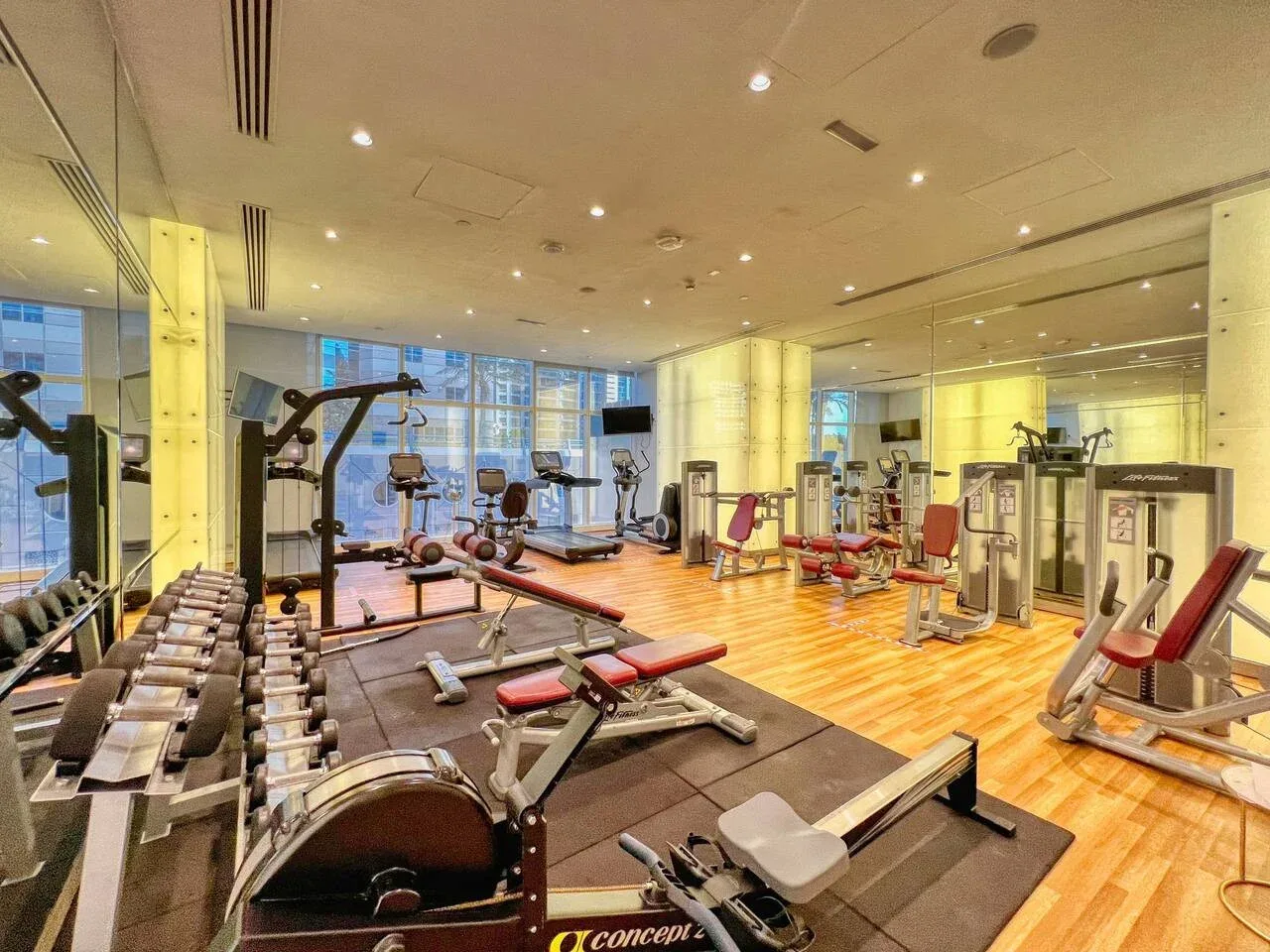 Un gimnasio con bancos de pesas, máquinas de ejercicio y una zona de entrenamiento con suelo de madera.