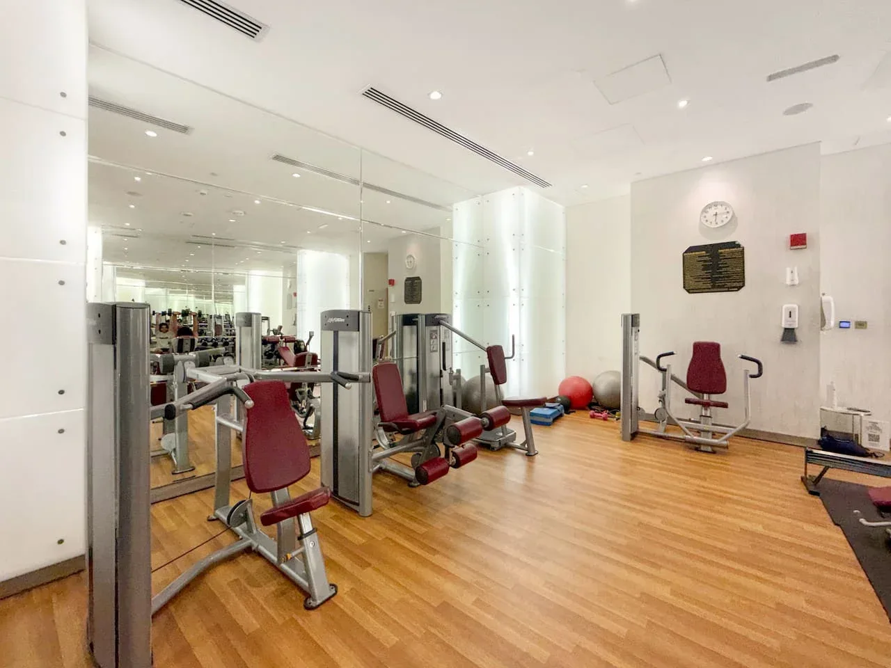Una sala de ejercicio luminosa con máquinas, asientos rojos y suelo de tono madera.
