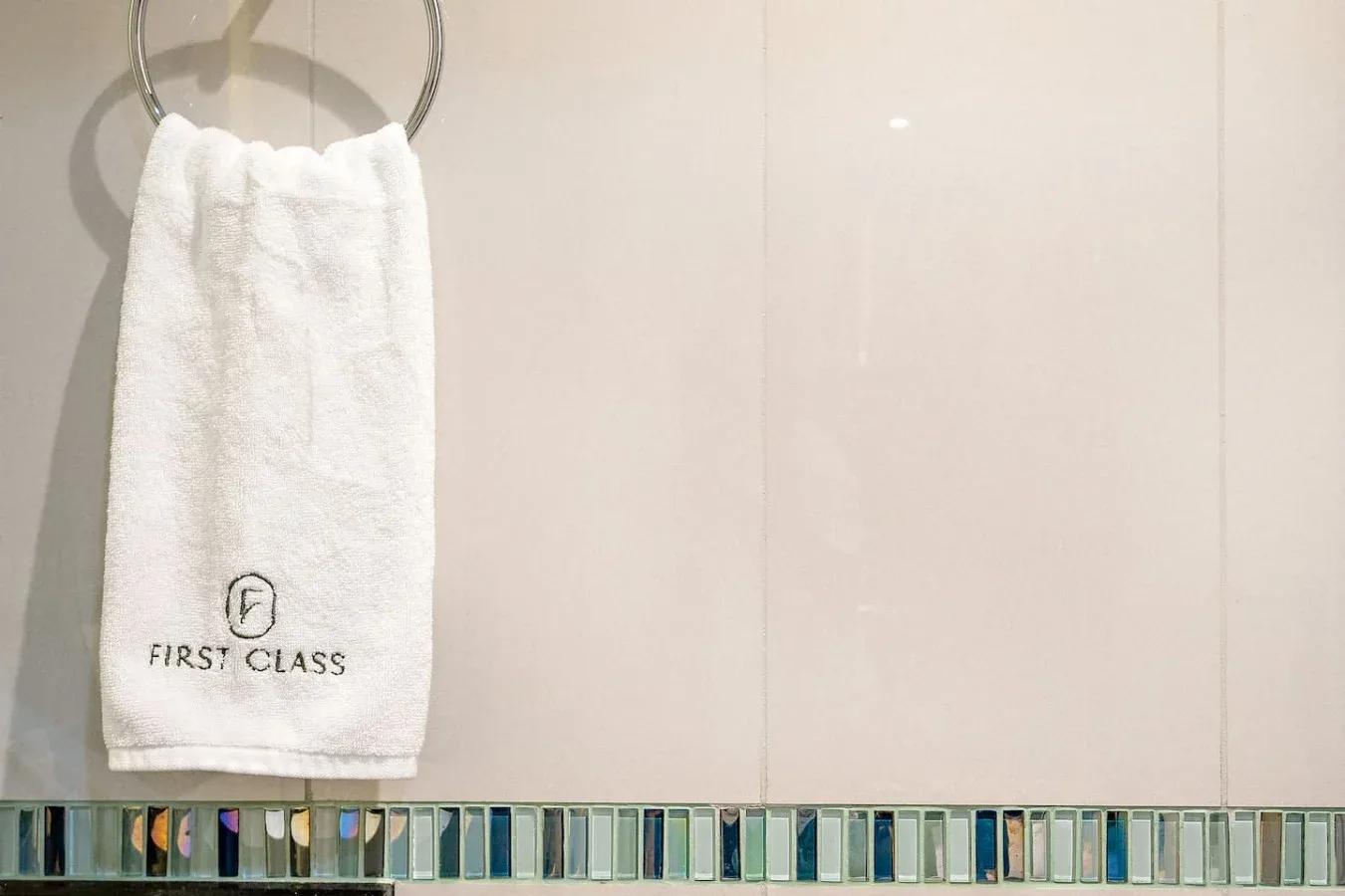 Una toalla blanca cuelga sobre una franja estrecha de azulejos decorativos en un baño.