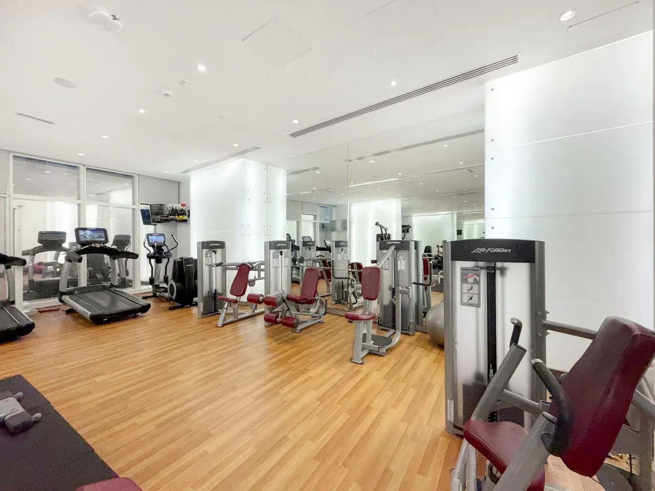 Un gimnasio luminoso con máquinas de ejercicio y cintas de correr sobre un suelo de aspecto de madera.