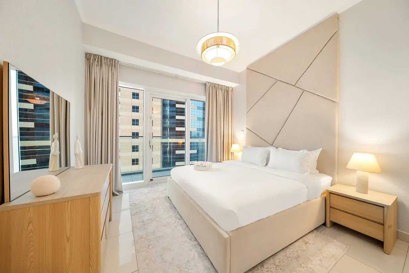 Un dormitorio luminoso con una cama grande, mesitas de noche y ventanas altas.