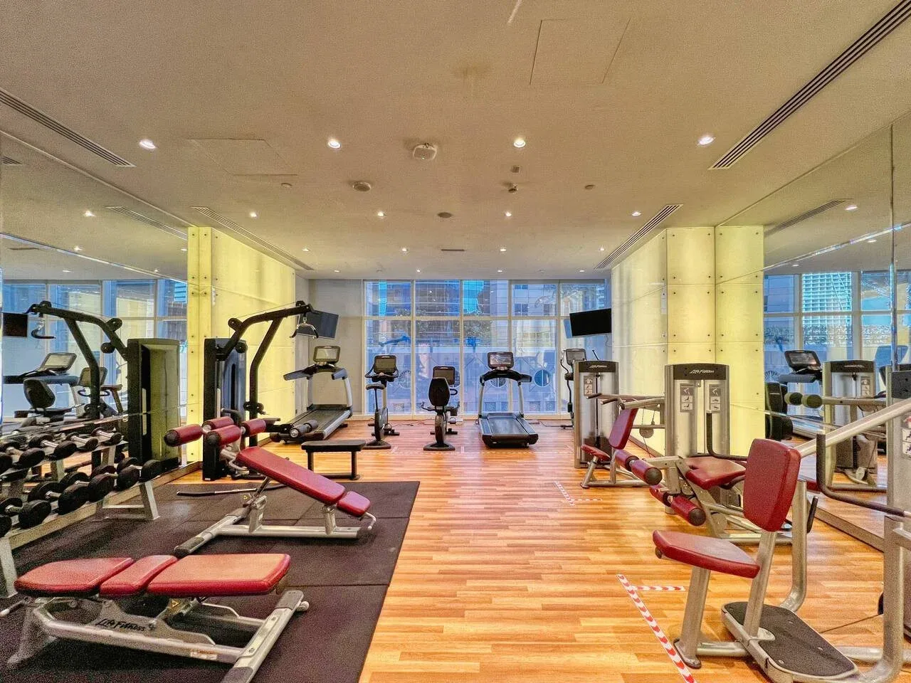 Un gimnasio con máquinas de ejercicio y bancos de pesas en una sala con suelo de madera.