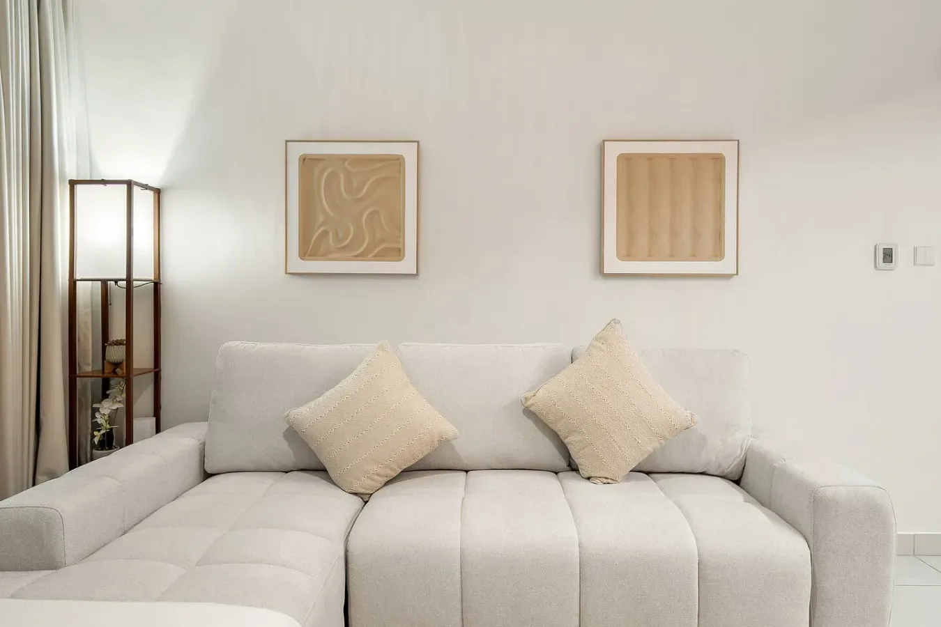 Una sala luminosa con un sofá seccional claro y dos cojines.