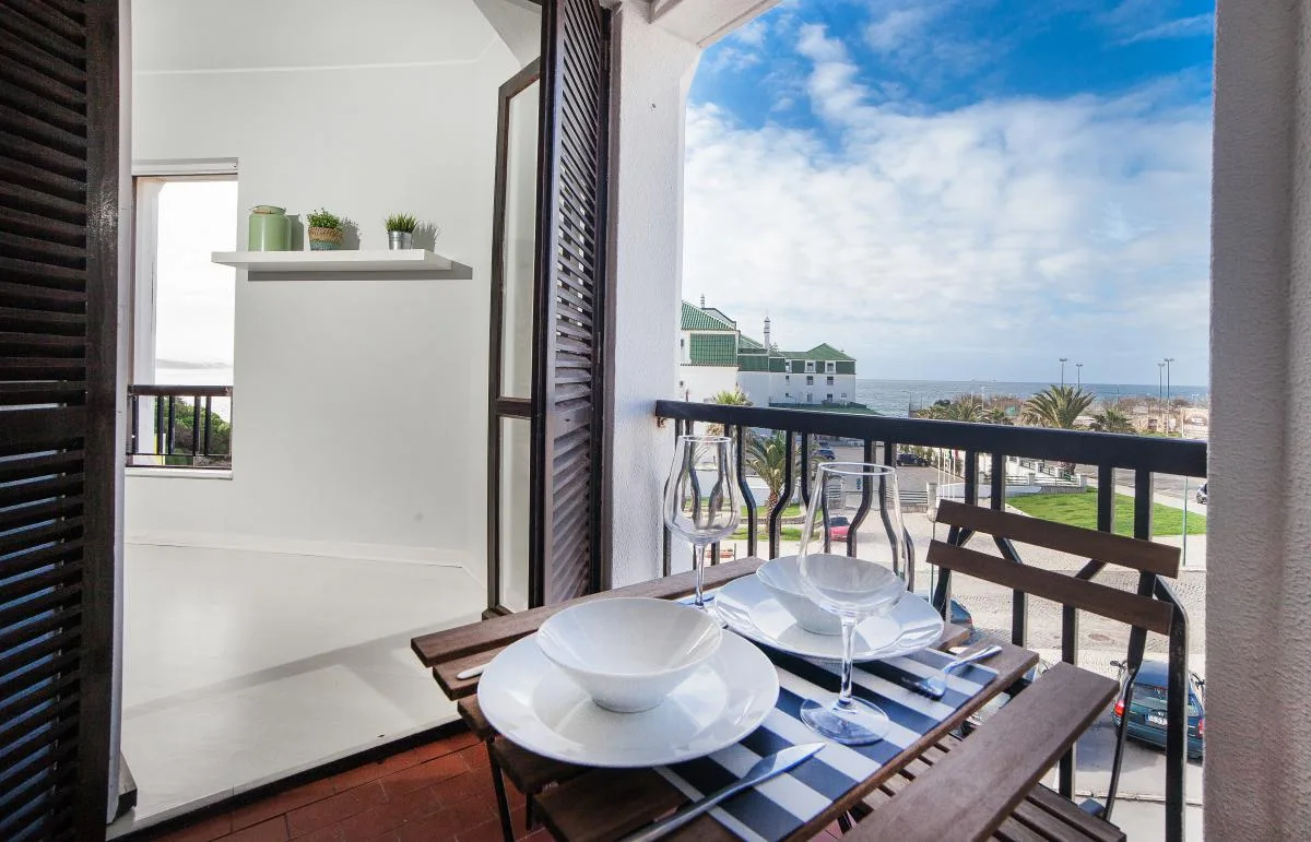 A small balcony dining area overlooks nearby buildings and the ocean.