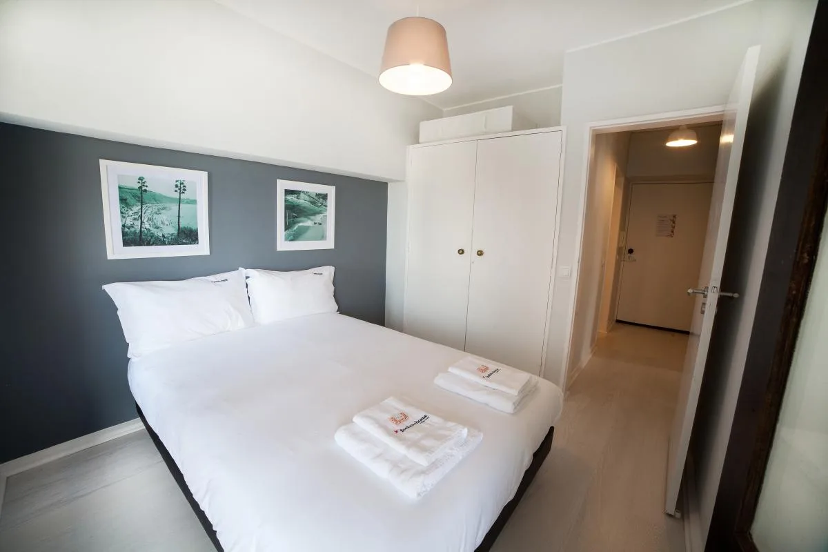 A bedroom with white bedding, framed pictures, and a built-in wardrobe.