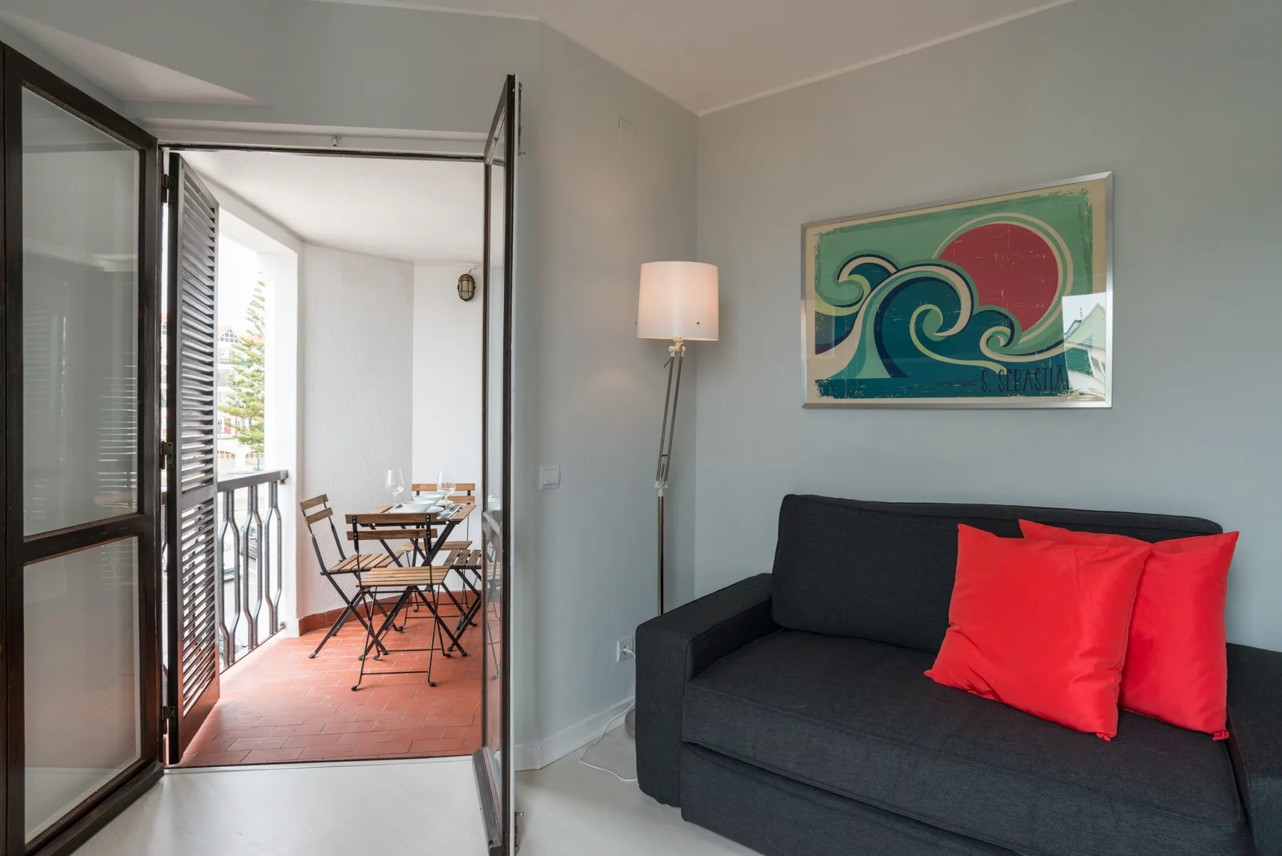 A living room with dark seating and a colorful wave painting beside an open balcony.