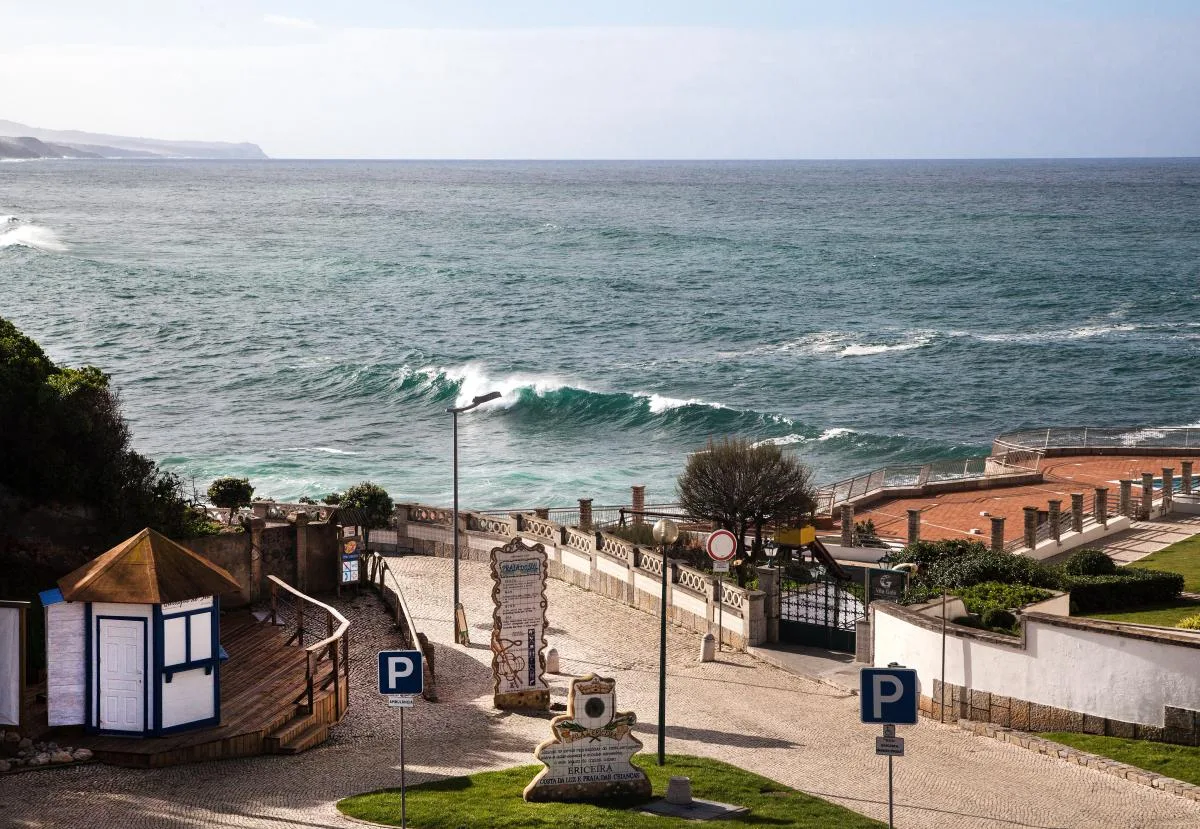 A coastal promenade overlooks the ocean, with waves breaking along the shore.