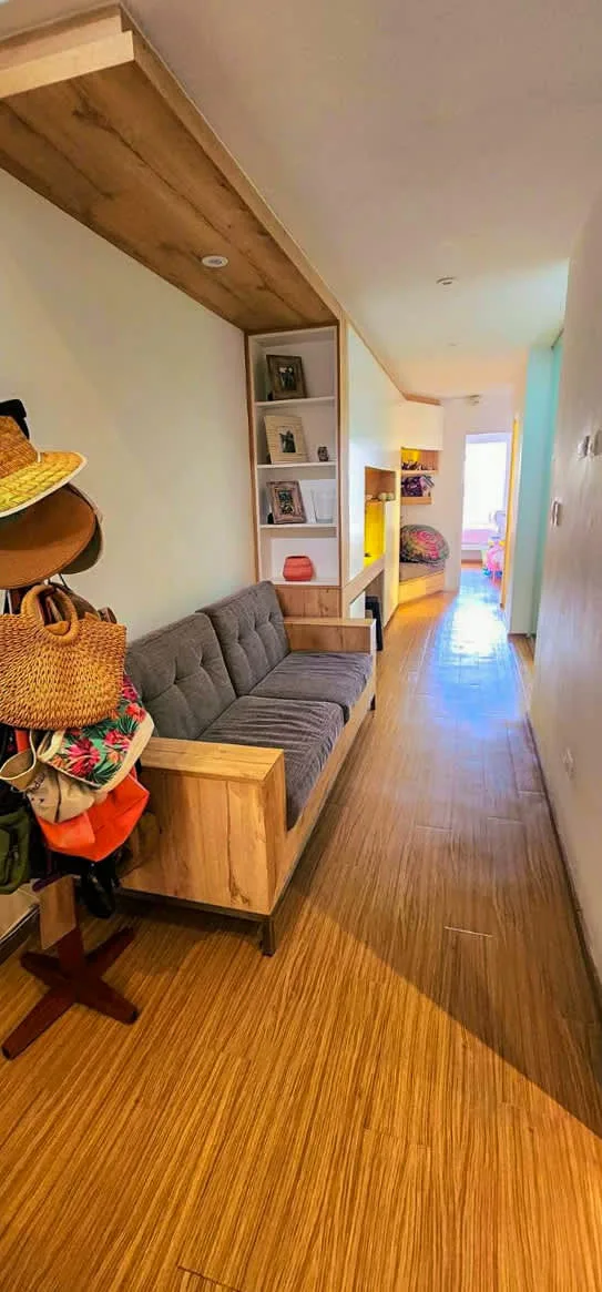 A narrow hallway has a gray upholstered bench, shelving, and wood flooring.