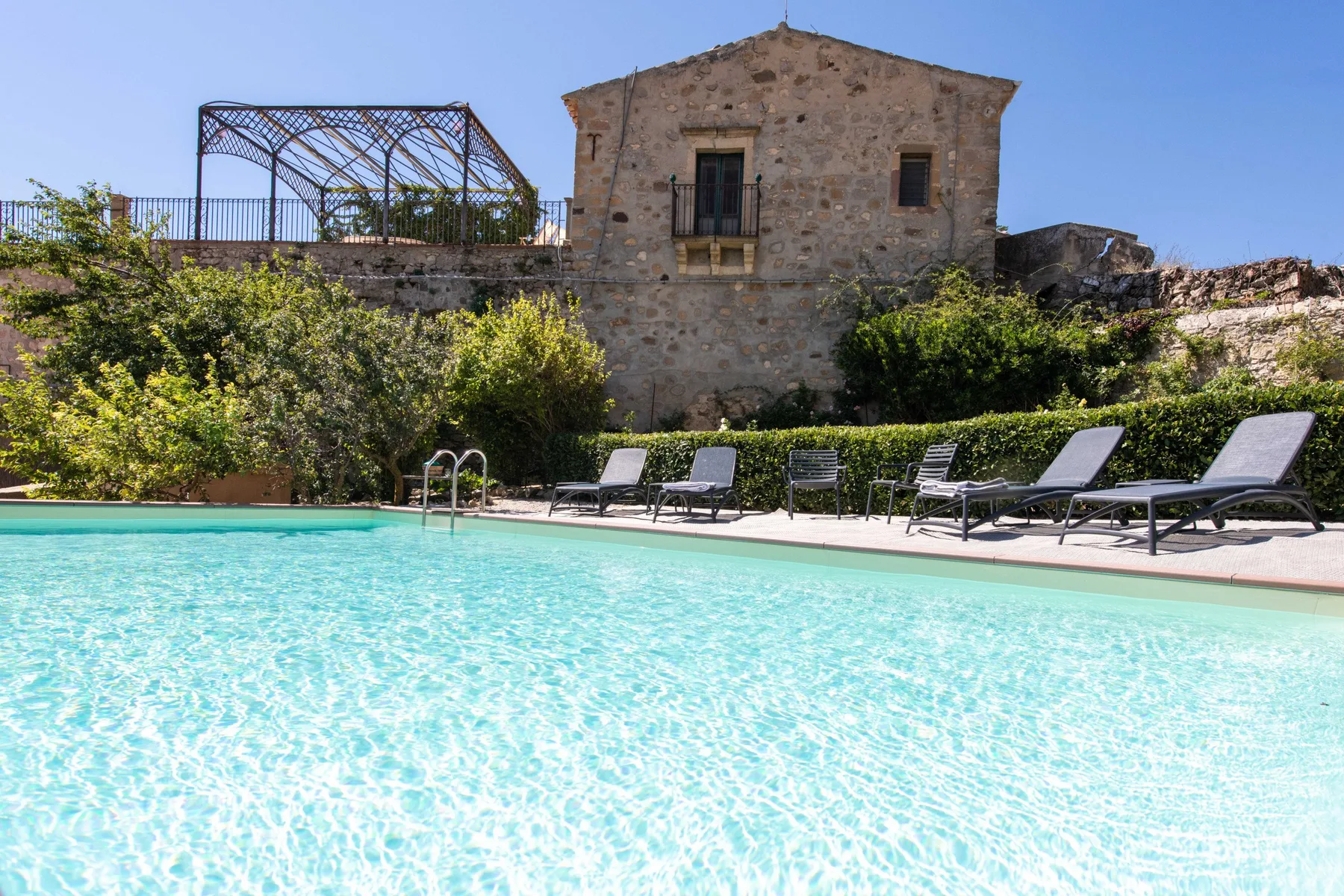Una piscina al aire libre está junto a asientos reclinables y un edificio de piedra.