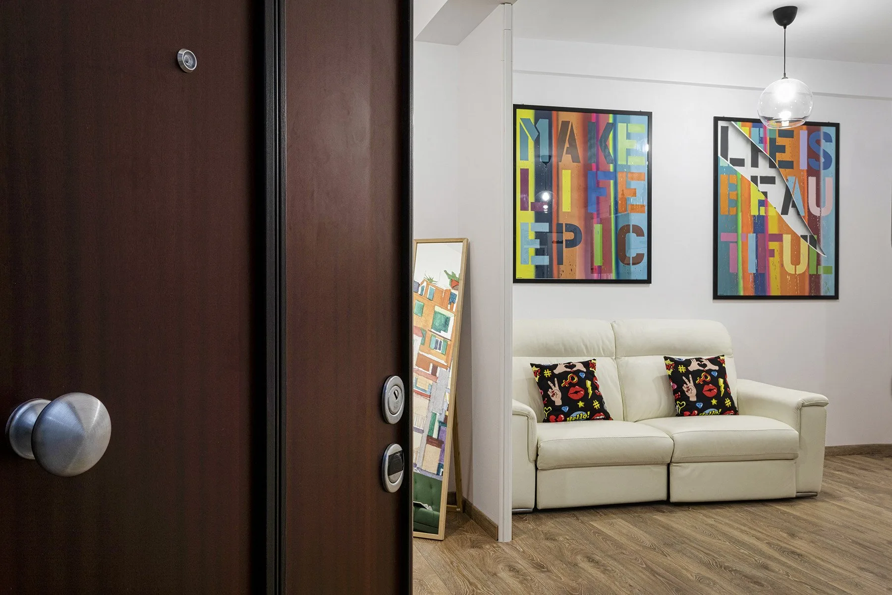 Sala de estar con un sofá claro y obras de arte coloridas enmarcadas.