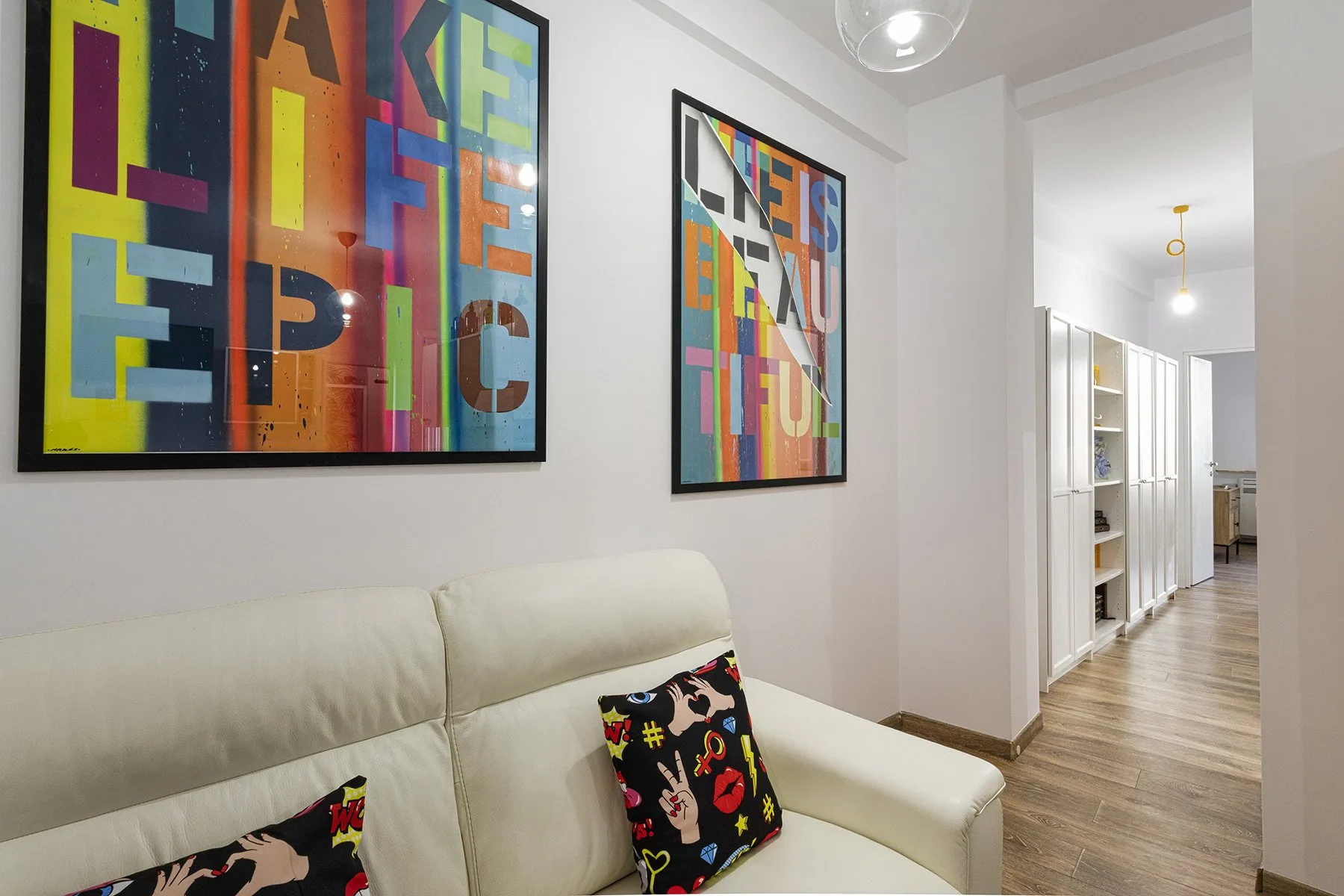 Una sala luminosa con un sofá color crema y cuadros coloridos enmarcados.